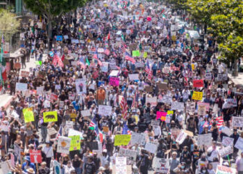 La gente agitando banderas y letreros de transporte llena una calle durante la protesta de No Kings