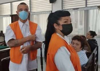 Tres personas con chalecos naranjas y caras faciales en lo que parece ser una audiencia judicial.