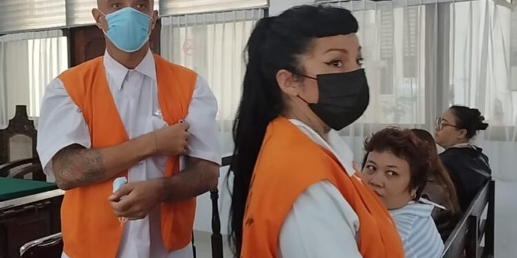 Tres personas con chalecos naranjas y caras faciales en lo que parece ser una audiencia judicial.