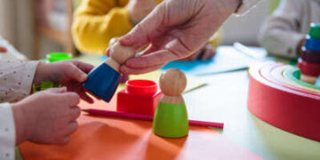 En un entorno de cuidado infantil, los niños juegan con juguetes y una mano para adultos, concéntrese en las manos