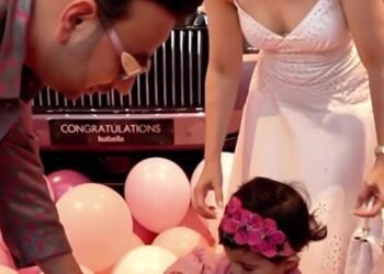 Una niña pequeña recibe una llave de automóvil de sus padres frente a un Rolls Royce rosa.