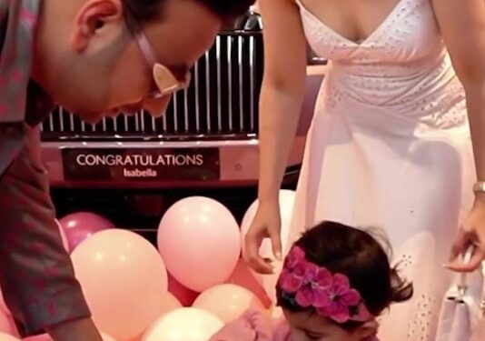 Una niña pequeña recibe una llave de automóvil de sus padres frente a un Rolls Royce rosa.