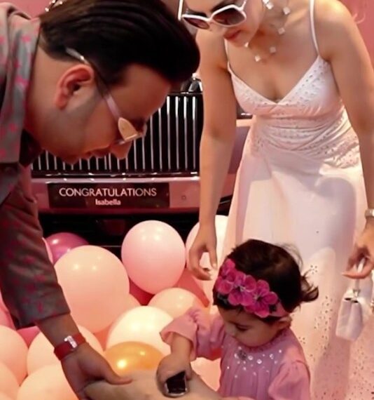 Una niña pequeña recibe una llave de automóvil de sus padres frente a un Rolls Royce rosa.