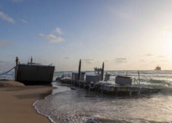 Un soldado estadounidense se encuentra en un buque militar estadounidense que encalló en una playa en la ciudad costera israelí de Ashdod el 25 de mayo de 2024. El ejército de los Estados Unidos dijo que cuatro de sus embarcaciones, apoyando un muelle temporal construido para entregar ayuda a Gaza por mar, se habían apresurado en mares pesados.