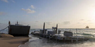 Un soldado estadounidense se encuentra en un buque militar estadounidense que encalló en una playa en la ciudad costera israelí de Ashdod el 25 de mayo de 2024. El ejército de los Estados Unidos dijo que cuatro de sus embarcaciones, apoyando un muelle temporal construido para entregar ayuda a Gaza por mar, se habían apresurado en mares pesados.