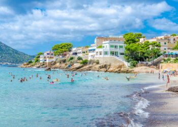 Escena de playa con gente nadando y relajándose en la orilla cerca de los edificios.