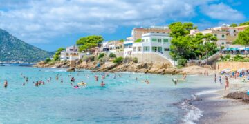 Escena de playa con gente nadando y relajándose en la orilla cerca de los edificios.