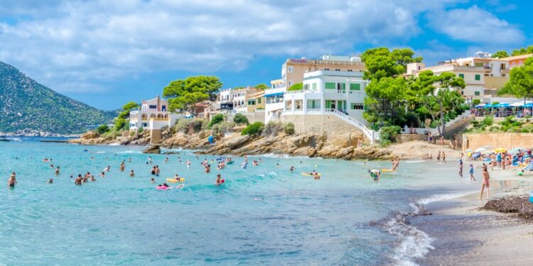 Escena de playa con gente nadando y relajándose en la orilla cerca de los edificios.
