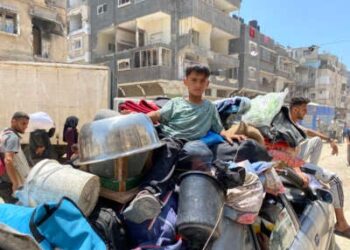 Un niño se sienta con pertenencias llenas y camas sobre un vehículo en movimiento mientras las personas desplazadas huyen de Khan Yunis hacia el oeste a Al-Mawasi en la Franja del Sur de Gaza el 3 de junio de 2025, después de que el ejército israelí emitió una orden de evacuación.