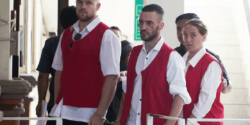 Tres personas en chalecos rojos y esposas.