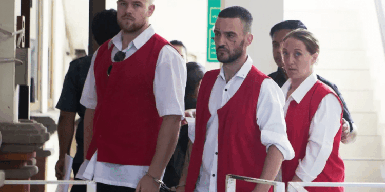 Tres personas en chalecos rojos y esposas.