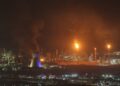 El humo y las llamas se elevan de una refinería de aceite por la noche.