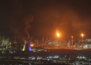 El humo y las llamas se elevan de una refinería de aceite por la noche.