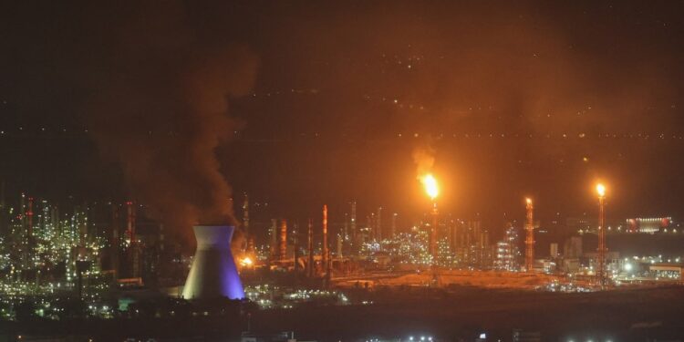 El humo y las llamas se elevan de una refinería de aceite por la noche.