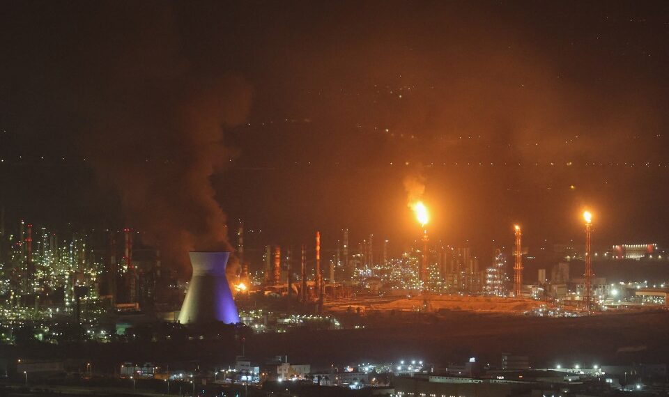 El humo y las llamas se elevan de una refinería de aceite por la noche.