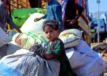 Un niño pequeño se agarra a una bolsa más grande que ella como hombres detrás de su carga un camión