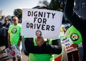 Una persona con una camisa verde sostiene un letrero que lee "Dignidad para conductores" con el logotipo de los conductores de viaje compartido debajo del texto