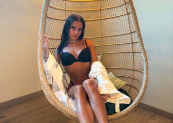 Mujer con top de bikini negro y túnica blanca sentada en una silla de mimbre.