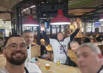 Un grupo de hombres en un bar de aeropuerto, un hombre está levantando las manos.