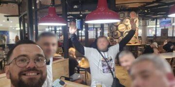 Un grupo de hombres en un bar de aeropuerto, un hombre está levantando las manos.