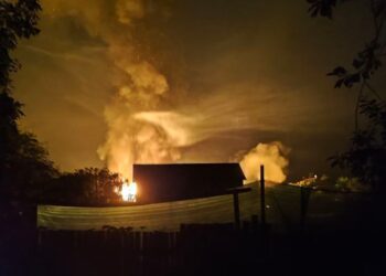 Vista nocturna de un gran incendio ardiendo cerca de un edificio.
