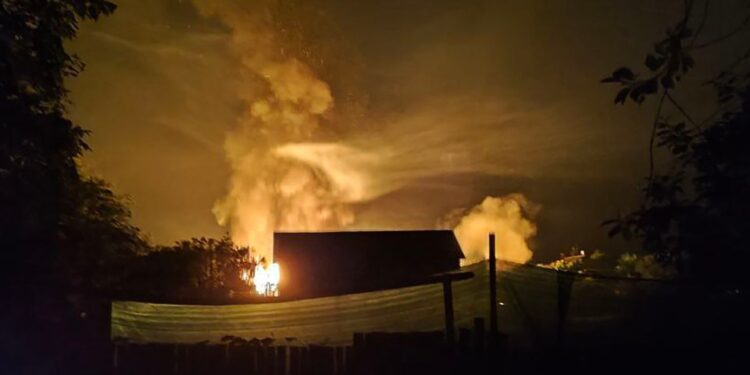 Vista nocturna de un gran incendio ardiendo cerca de un edificio.