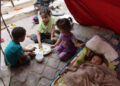 Los niños palestinos comparten una comida de arroz mientras un bebé duerme, dentro de una tienda de campaña en un campamento de desplazamiento cerca del puerto de la ciudad de Gaza el 22 de mayo de 2025.