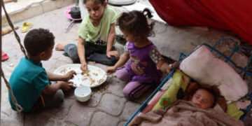 Los niños palestinos comparten una comida de arroz mientras un bebé duerme, dentro de una tienda de campaña en un campamento de desplazamiento cerca del puerto de la ciudad de Gaza el 22 de mayo de 2025.
