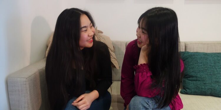 Dos mujeres jóvenes sentadas en un sofá, hablando.