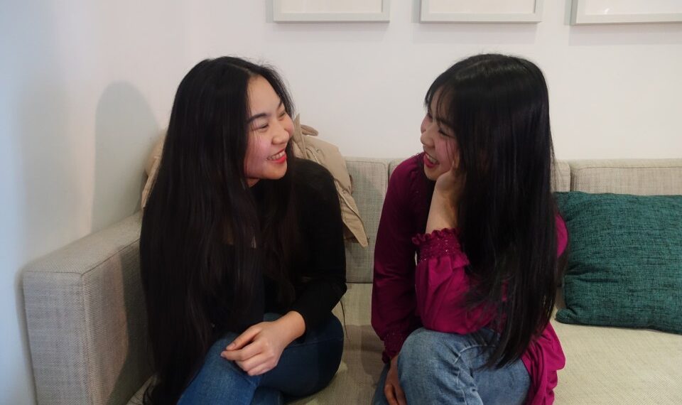 Dos mujeres jóvenes sentadas en un sofá, hablando.