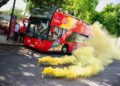 Un autobús turístico de dos pisos rodeado de bombas de humo amarillas.