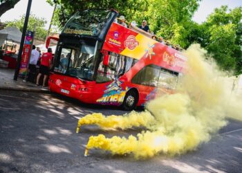 Un autobús turístico de dos pisos rodeado de bombas de humo amarillas.