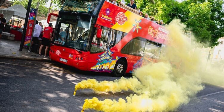 Un autobús turístico de dos pisos rodeado de bombas de humo amarillas.