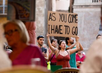 Manifestante sosteniendo un letrero que dice "Como vengo, tengo que irme" Frente a los turistas.