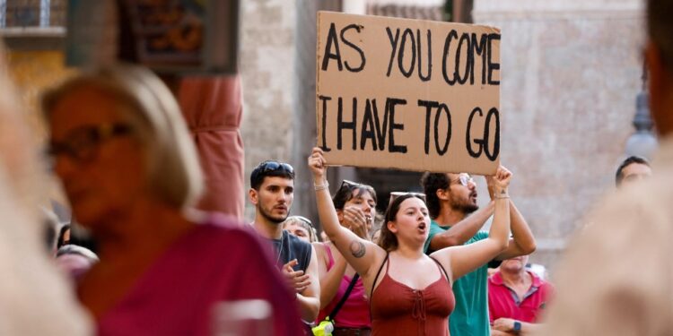 Manifestante sosteniendo un letrero que dice "Como vengo, tengo que irme" Frente a los turistas.