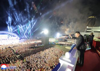 Kim Jong Un saluda a una gran multitud en una ceremonia nocturna con fuegos artificiales.