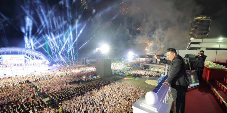 Kim Jong Un saluda a una gran multitud en una ceremonia nocturna con fuegos artificiales.