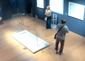 Vista de gran ángulo de dos personas en una galería de arte cerca de una instalación de arte dañada.