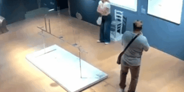 Vista de gran ángulo de dos personas en una galería de arte cerca de una instalación de arte dañada.