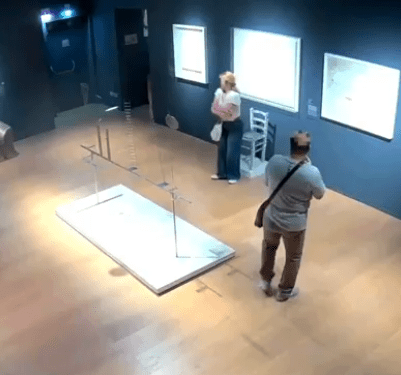 Vista de gran ángulo de dos personas en una galería de arte cerca de una instalación de arte dañada.