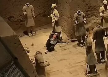 Una persona sentada entre las estatuas del ejército de terracota dañada.