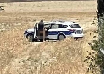 Dos policías que participan en actividades sexuales cerca de un automóvil policial.