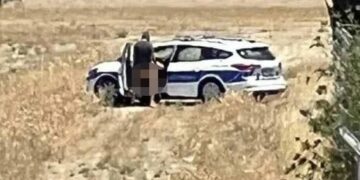 Dos policías que participan en actividades sexuales cerca de un automóvil policial.