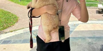 Mujer sosteniendo un perro pequeño y dando un signo de paz.