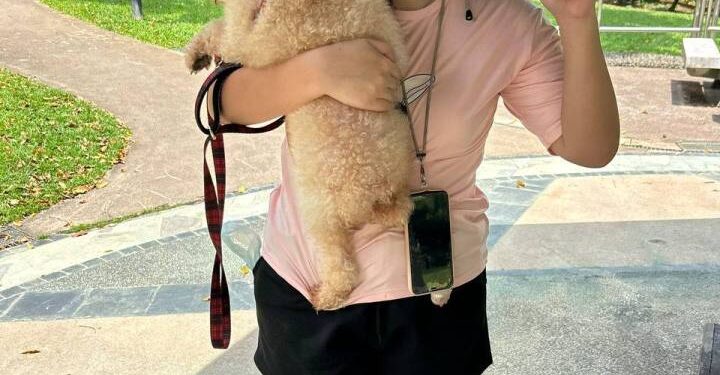 Mujer sosteniendo un perro pequeño y dando un signo de paz.