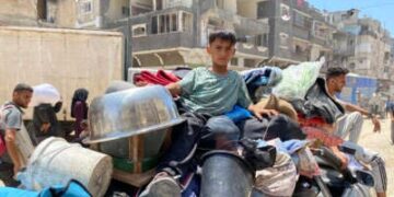 Un niño se sienta con pertenencias llenas y camas sobre un vehículo en movimiento mientras las personas desplazadas huyen de Khan Yunis hacia el oeste a Al-Mawasi en la Franja del Sur de Gaza el 3 de junio de 2025, después de que el ejército israelí emitió una orden de evacuación.