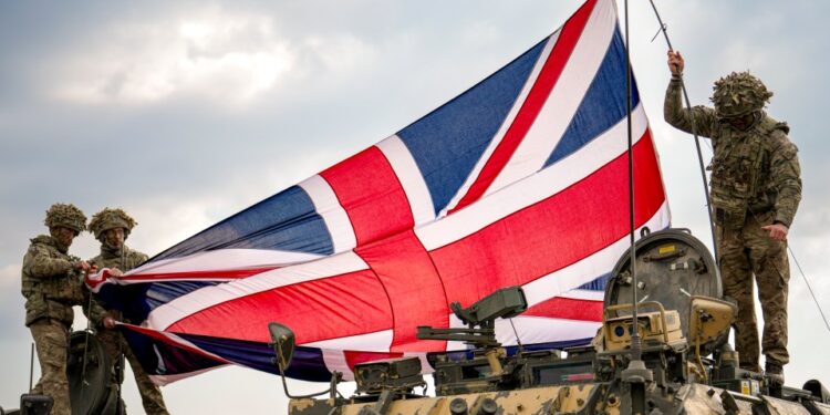 Soldados colocando una bandera británica en un vehículo militar.