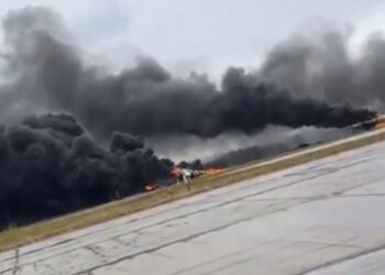 Gran columna de humo negro que se eleva desde un aeródromo en llamas.