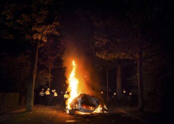 Un auto en llamas durante un motín, con policías que estaban de pie.