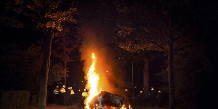 Un auto en llamas durante un motín, con policías que estaban de pie.